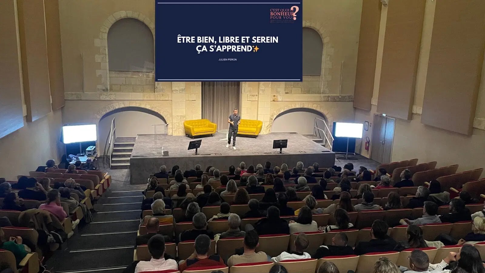 Julien Peron sur scène dans une salle voûtée en pierre, lors d'un précédent congrès C'est quoi le bonheur pour vous ?